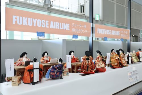 「FUKUYOSE AIRLINE」のチェックインカウンターで搭乗手続きをする雛人形（展示場所④）